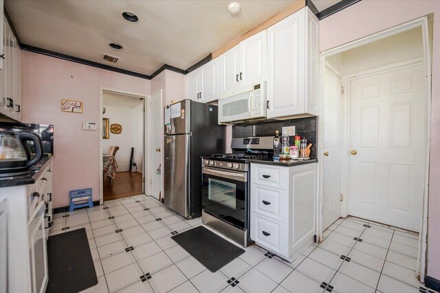 kitchen featuring visible vents, dark countertops, white cabinetry, stainless steel appliances, and decorative backsplash