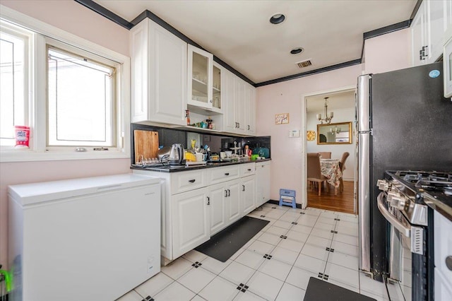 kitchen featuring stainless steel gas range oven, glass insert cabinets, refrigerator, and white cabinets