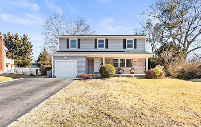 traditional-style home with a front lawn, aphalt driveway, fence, an attached garage, and brick siding