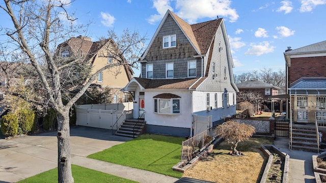 shingle-style home featuring stucco siding, roof with shingles, driveway, and fence