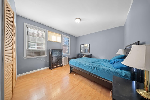 bedroom with radiator heating unit, wood finished floors, baseboards, and a closet