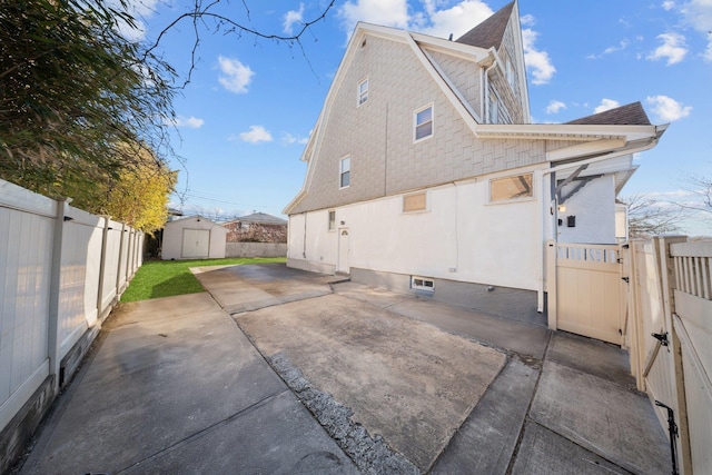 view of home's exterior featuring an outbuilding, a fenced backyard, a gambrel roof, a storage unit, and a patio area