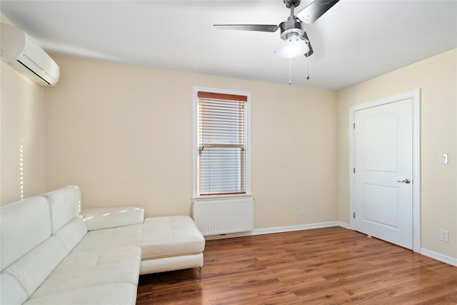 sitting room featuring baseboards, an AC wall unit, radiator heating unit, wood finished floors, and a ceiling fan