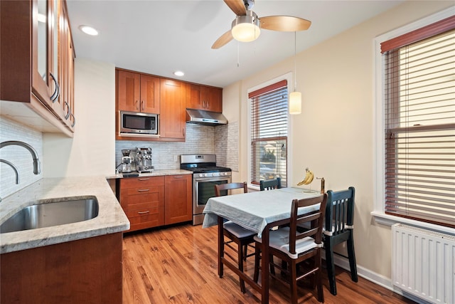 kitchen featuring radiator, a sink, stainless steel appliances, extractor fan, and brown cabinets