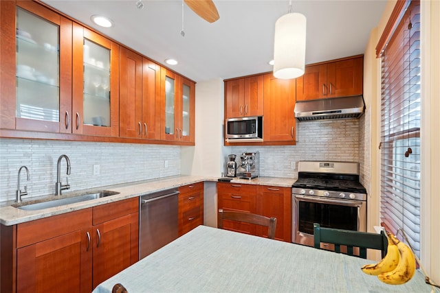 kitchen with brown cabinets, under cabinet range hood, a sink, appliances with stainless steel finishes, and glass insert cabinets