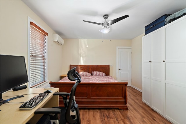 bedroom with a ceiling fan, wood finished floors, and a wall mounted air conditioner