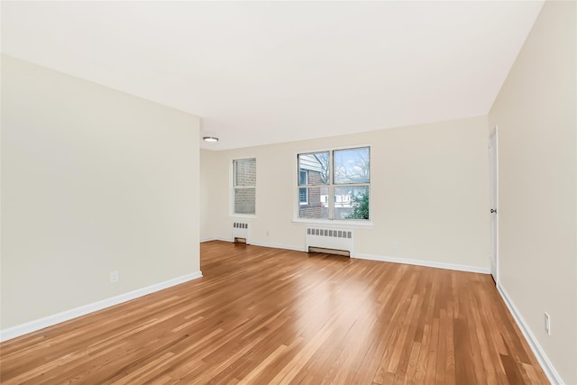 empty room with light wood-style flooring, radiator heating unit, and baseboards