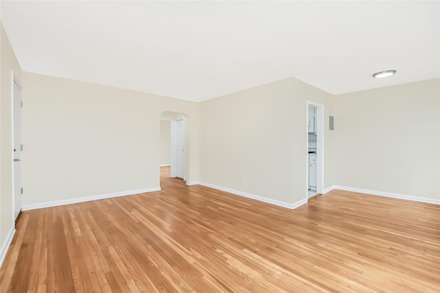 unfurnished room with arched walkways, baseboards, and light wood-style floors