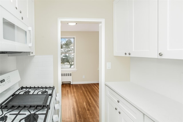 kitchen with wood finished floors, radiator heating unit, white appliances, white cabinets, and light countertops