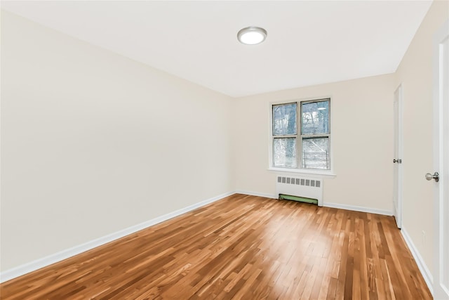 empty room featuring baseboards, radiator heating unit, and light wood finished floors