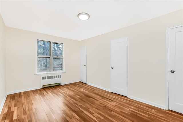 spare room with radiator heating unit, wood finished floors, and baseboards