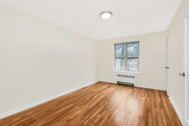 spare room with baseboards, radiator heating unit, and light wood-style floors