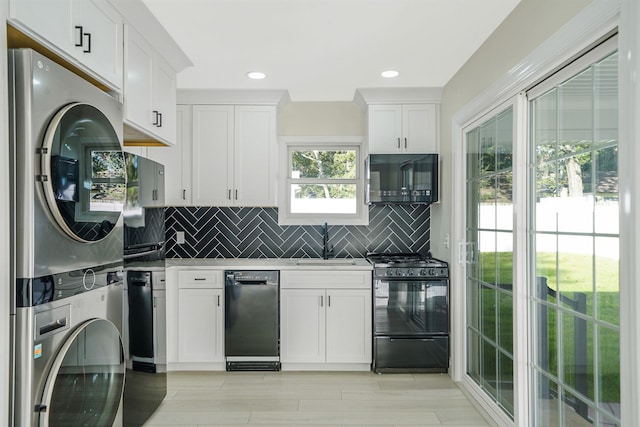 kitchen featuring a sink, white cabinetry, black appliances, and stacked washer and dryer