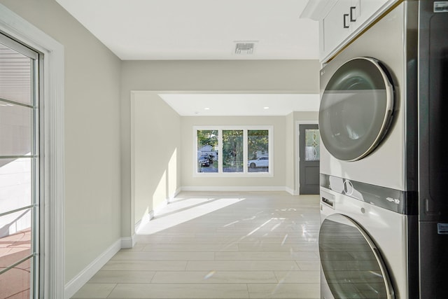 washroom with light wood-type flooring, visible vents, baseboards, and stacked washing maching and dryer