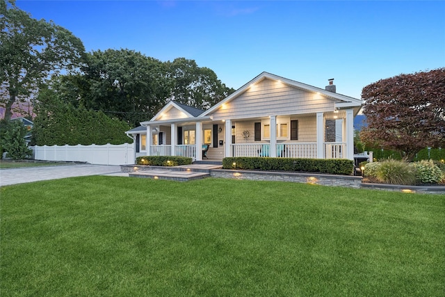 view of front facade featuring driveway, a front lawn, a porch, fence, and a chimney