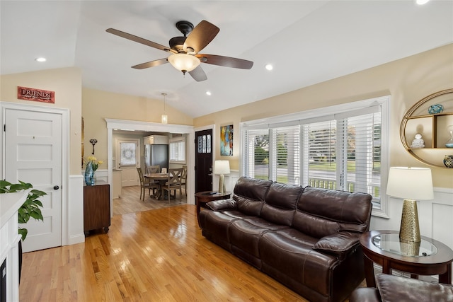 living area featuring a wainscoted wall, light wood-style flooring, a ceiling fan, and vaulted ceiling