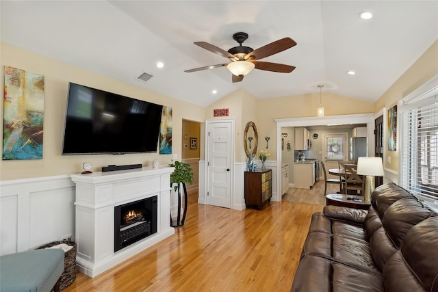 living area with light wood-type flooring, lofted ceiling, visible vents, and wainscoting