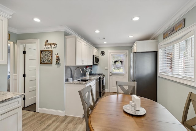 kitchen featuring light wood-type flooring, ornamental molding, a sink, white cabinetry, and appliances with stainless steel finishes