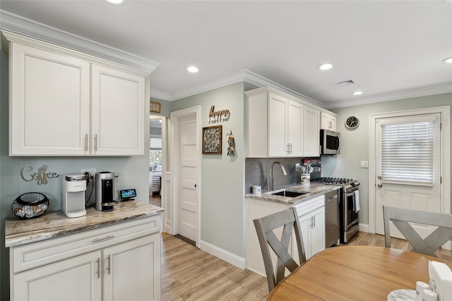 kitchen featuring visible vents, a sink, stainless steel appliances, crown molding, and light wood finished floors