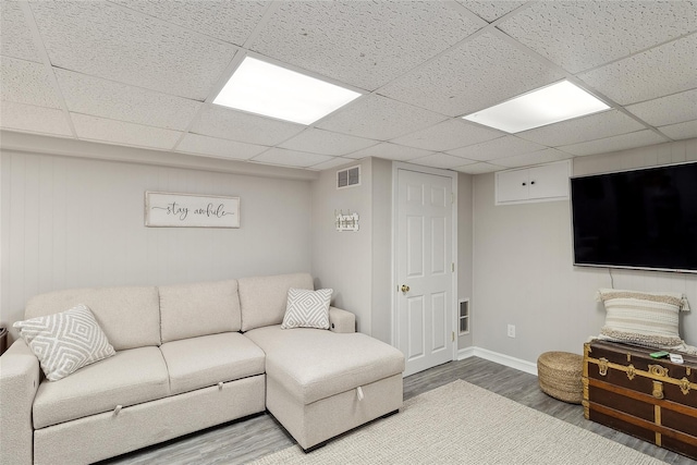 living area with wood finished floors, visible vents, a drop ceiling, and baseboards