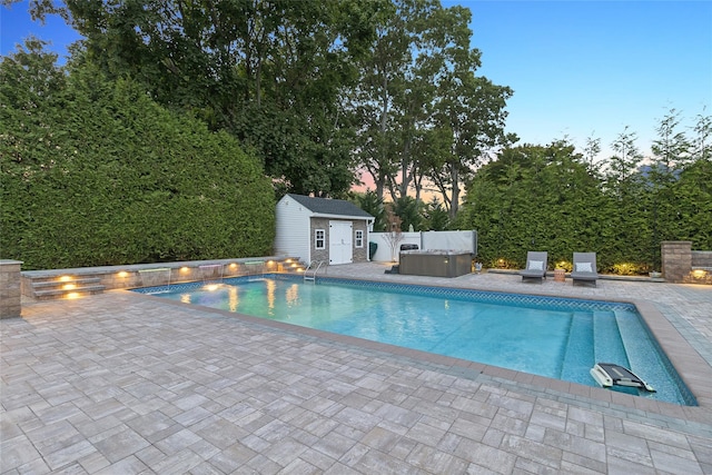 pool at dusk featuring an outbuilding, a hot tub, a storage shed, and a patio