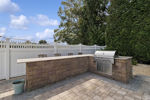 view of patio with an outdoor kitchen, a fenced backyard, and a grill