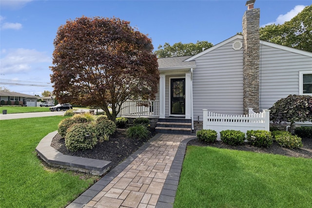 exterior space featuring a yard, a porch, a chimney, and a shingled roof