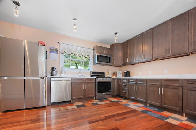 kitchen with stainless steel appliances, dark brown cabinetry, wood finished floors, and light countertops