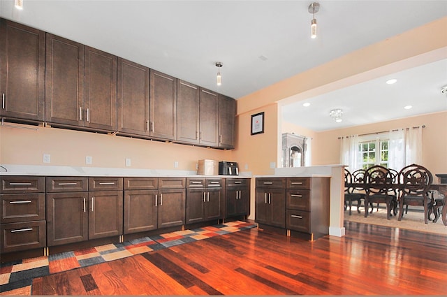 kitchen with dark brown cabinets, a peninsula, light countertops, and dark wood-style flooring