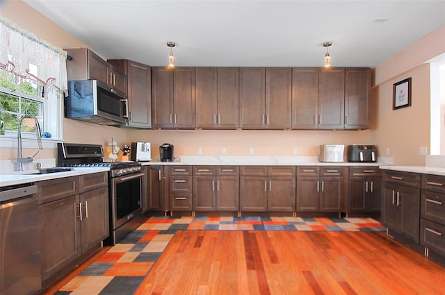 kitchen featuring a sink, stainless steel appliances, light countertops, dark brown cabinets, and hanging light fixtures