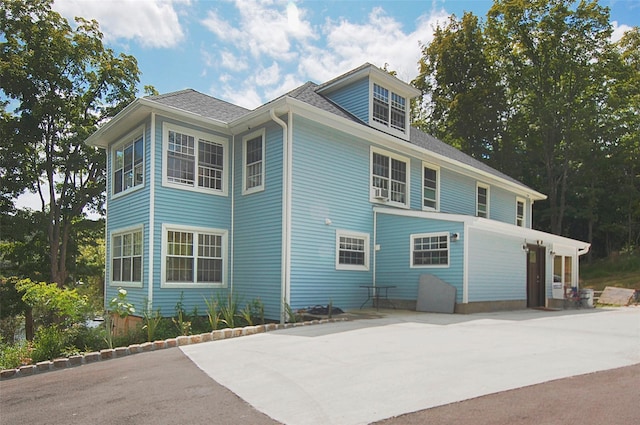 view of side of home featuring a shingled roof, concrete driveway, and a patio area