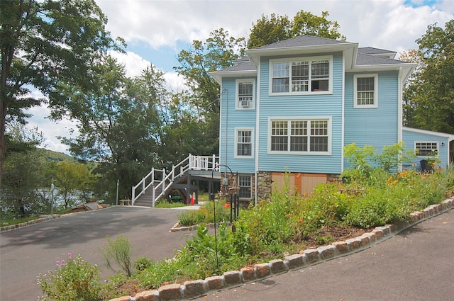 view of front of property featuring aphalt driveway, stone siding, and stairs