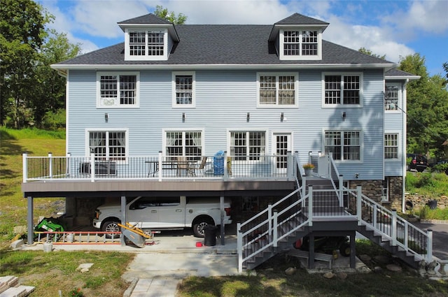 rear view of property with a deck, stairs, driveway, and a shingled roof