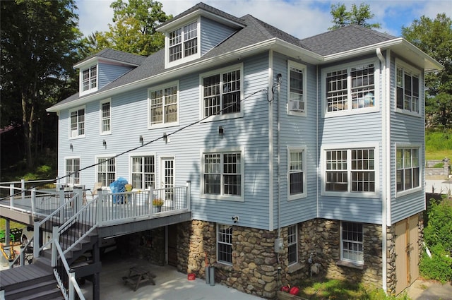 rear view of property with a patio, a deck, stairs, and a shingled roof