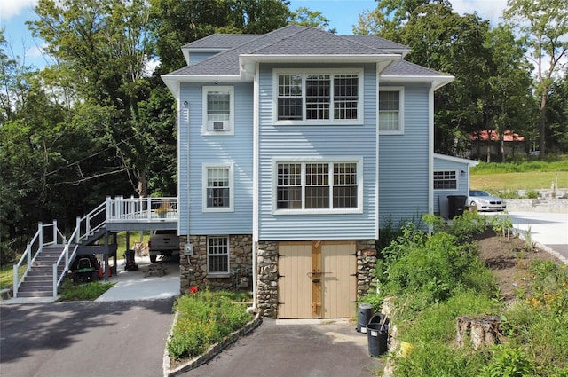 view of front of home featuring stairway, roof with shingles, stone siding, a deck, and aphalt driveway