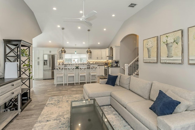 living area with visible vents, light wood-style floors, ceiling fan, and high vaulted ceiling