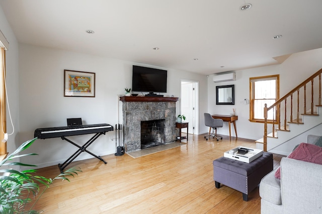 living area featuring baseboards, stairway, a wall mounted air conditioner, light wood-type flooring, and a fireplace