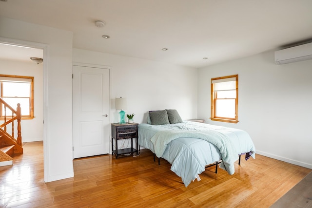 bedroom with light wood finished floors, recessed lighting, a wall mounted air conditioner, and baseboards