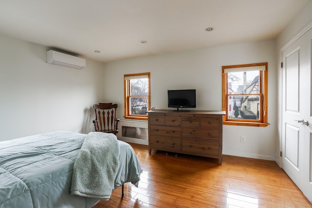 bedroom with a wall unit AC, light wood-style flooring, recessed lighting, and baseboards