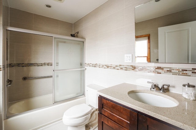 bathroom with backsplash, tile walls, toilet, enclosed tub / shower combo, and vanity