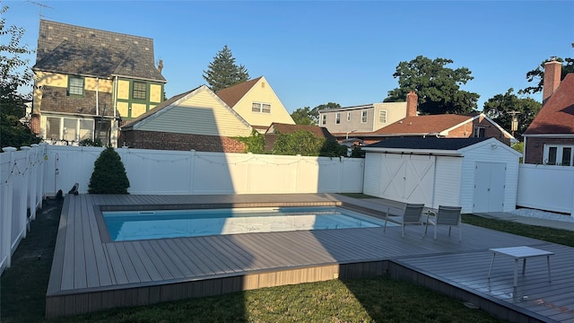 view of pool with a fenced in pool, a fenced backyard, a deck, an outbuilding, and a storage unit