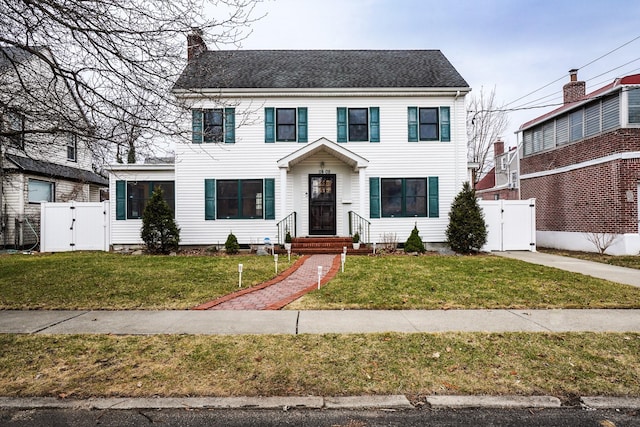 colonial-style house with fence, a chimney, a front lawn, and a gate