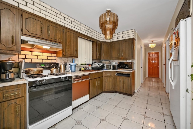 kitchen featuring under cabinet range hood, range with gas cooktop, light countertops, and freestanding refrigerator