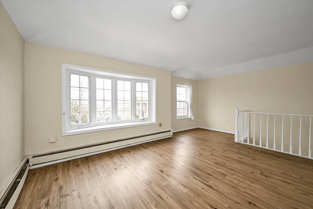 spare room featuring a baseboard heating unit, wood finished floors, and baseboards