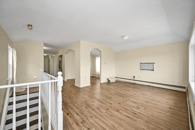 unfurnished room featuring arched walkways, baseboard heating, light wood-style flooring, and baseboards