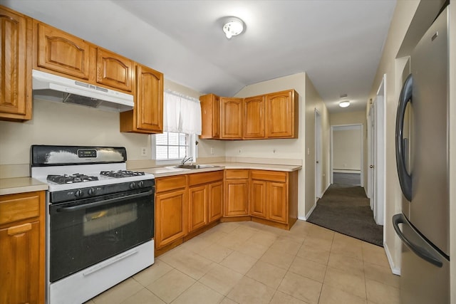 kitchen featuring white gas stove, under cabinet range hood, a sink, freestanding refrigerator, and light countertops