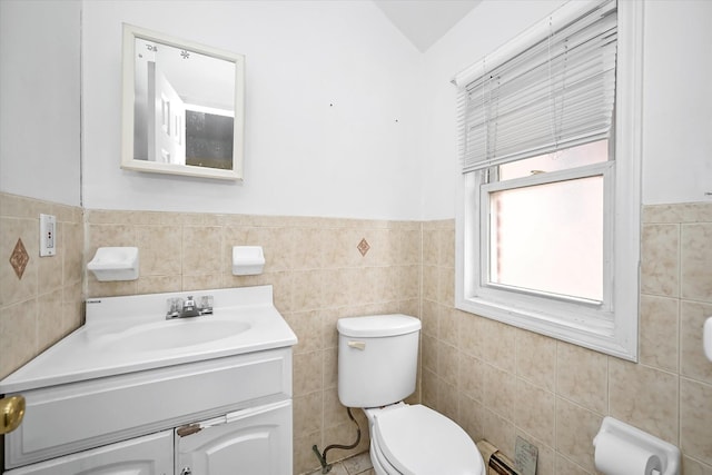 bathroom with a wainscoted wall, toilet, tile walls, and vanity