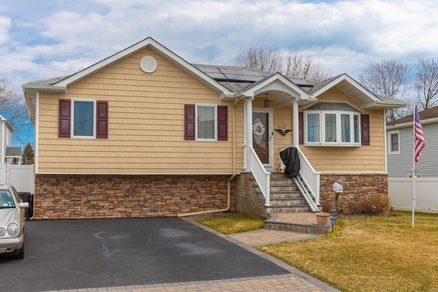 view of front of house with stone siding, solar panels, a front lawn, and fence