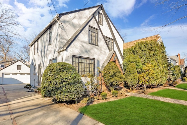 view of front of house with stucco siding, a garage, an outdoor structure, and a front lawn