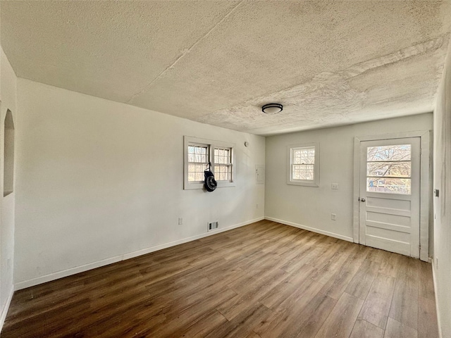 empty room with visible vents, a textured ceiling, wood finished floors, arched walkways, and baseboards